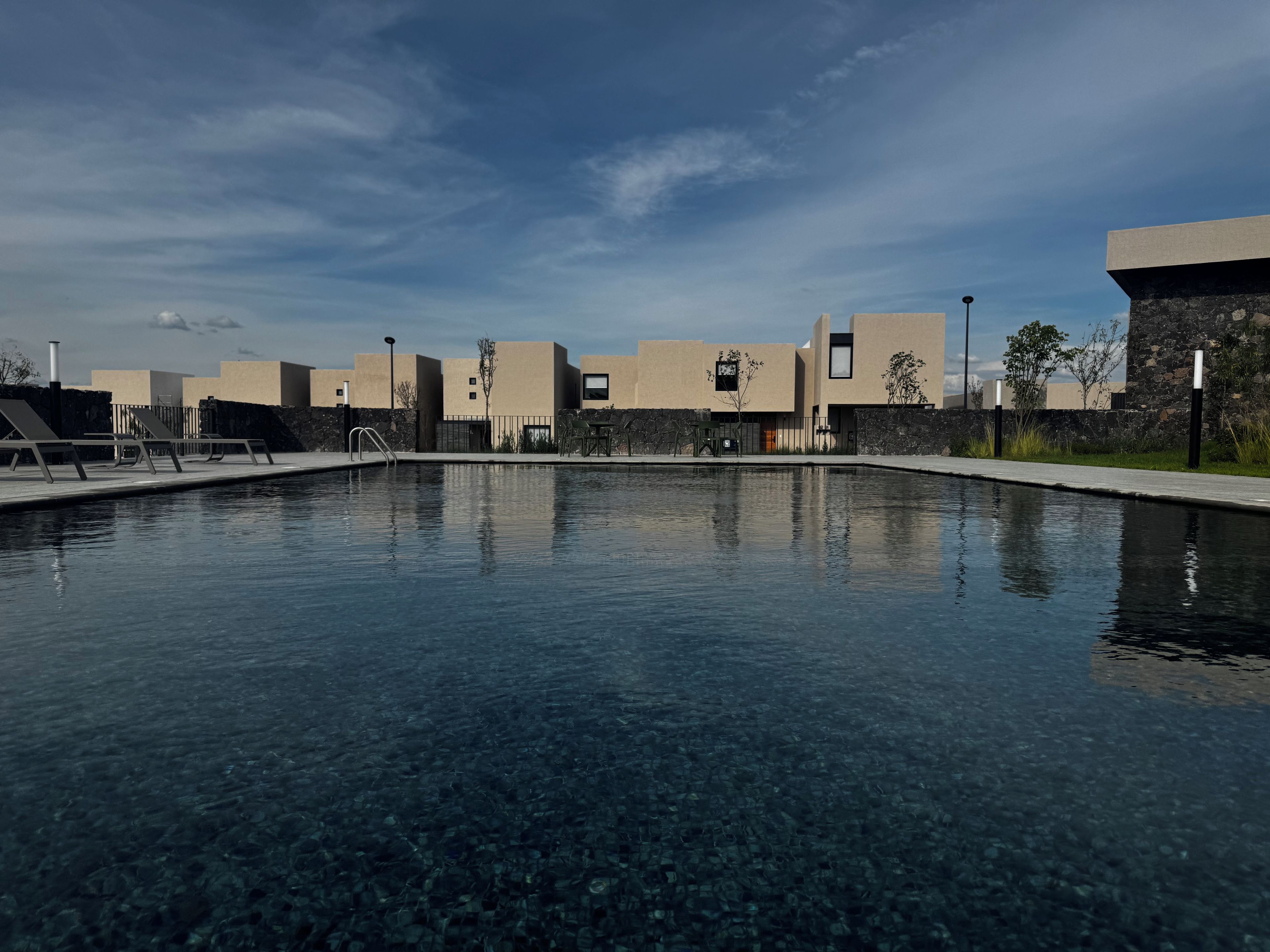 A swimming pool with clear water, surrounded by modern buildings and a stone wall.