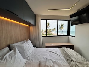 A modern bedroom with a large bed, a bedside table, and a view of the beach. - New Listing (Ipojuca)