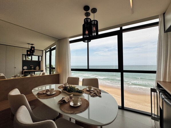 A modern dining area with a large window overlooking the ocean, a white table with placemats, and a minimalist interior design. - New Listing (Ipojuca)