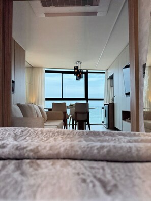 A modern hotel room with a large window, a sofa, a dining table, and a TV. - New Listing (Ipojuca)