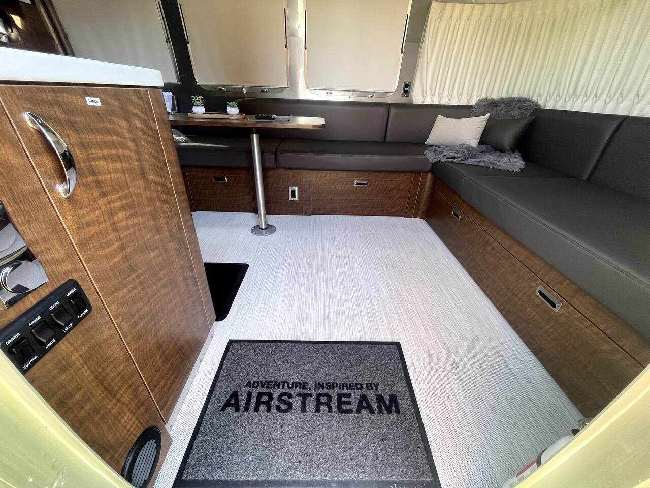 Ein kompaktes Wohnmobil-Interieur mit einer Küchenzeile, einer Sitzecke und einer Tür mit der Aufschrift 'TRASH'.