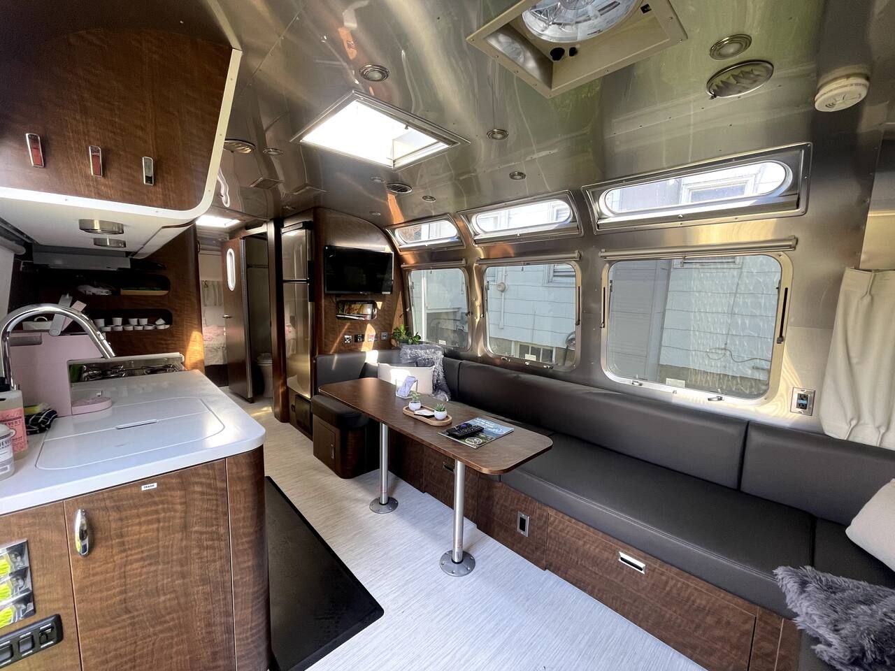 Ein kompaktes Wohnmobil-Interieur mit Küchenzeile, Essbereich und Sitzgelegenheit mit Fenstern.