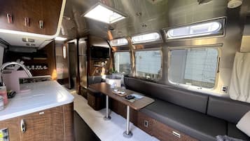 Ein kompaktes Wohnmobil-Interieur mit Küchenzeile, Essbereich und Sitzgelegenheit mit Fenstern.
