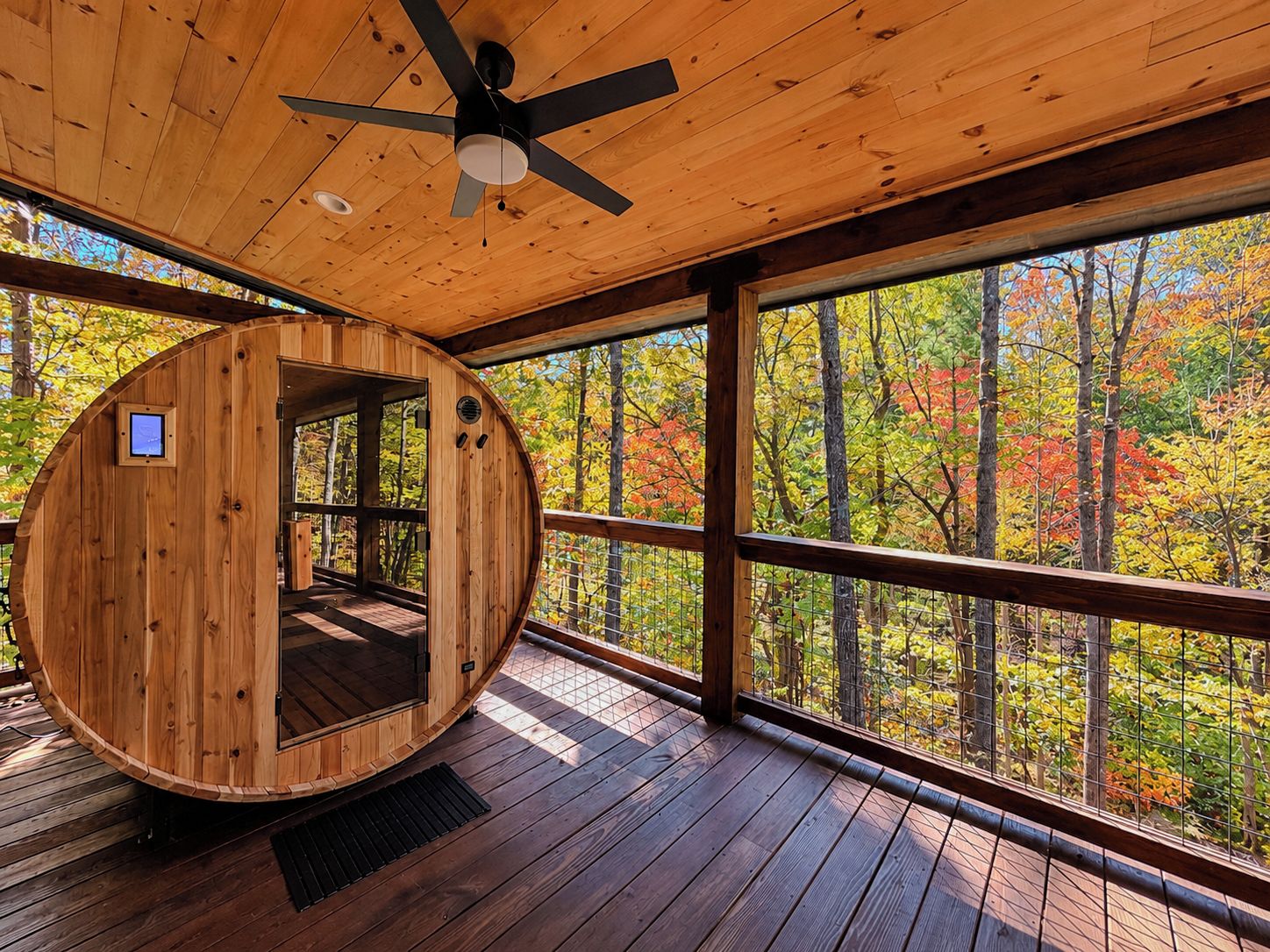 A wooden sauna with a curved exterior, large windows, and a ceiling fan.