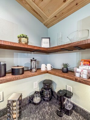 Una cocina con estantes de madera, una cafetera y diversos utensilios.