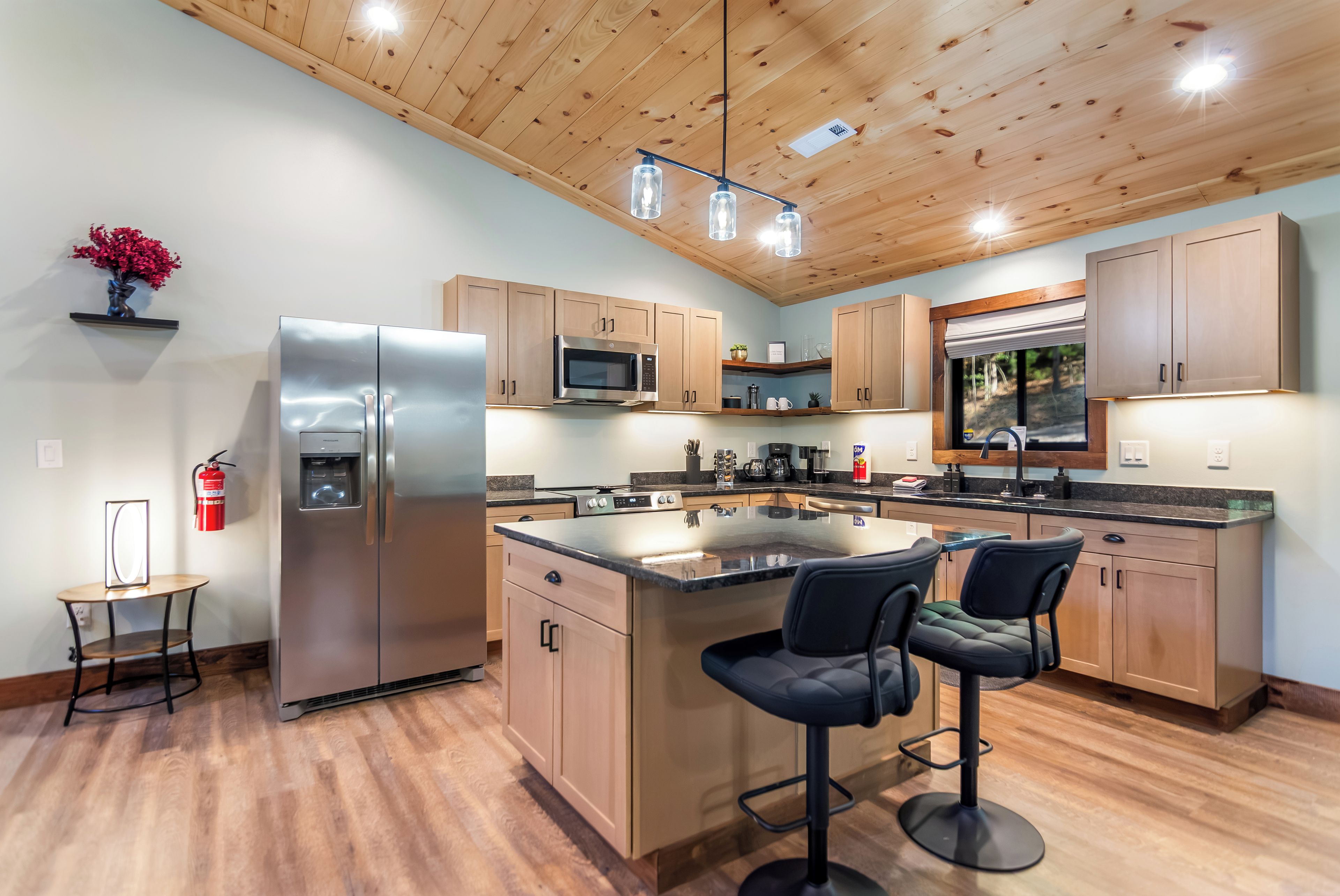 Una cocina moderna con armarios de madera, electrodomésticos de acero inoxidable, una isla central con taburetes y un techo con vigas a la vista.