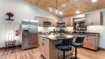 Una cocina moderna con armarios de madera, electrodomésticos de acero inoxidable, una isla central con taburetes y un techo con vigas a la vista.
