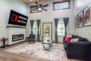 A living room with a fireplace, a ceiling fan, and a television mounted on the wall. - Romantic Adults Only Couples Escape - Play Room, VIP Room, and More (Mineral Bluff)