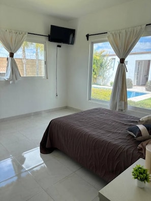 Un dormitorio con cama, televisor montado en la pared y ventana con cortinas.
