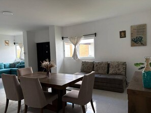 Un comedor con mesa y sillas de madera, un sofá y una ventana con cortinas.