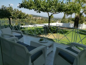 A patio with wicker furniture and a view of a green landscape. - Mythos luxury ground-floor apartment 3 (Kerkyra)