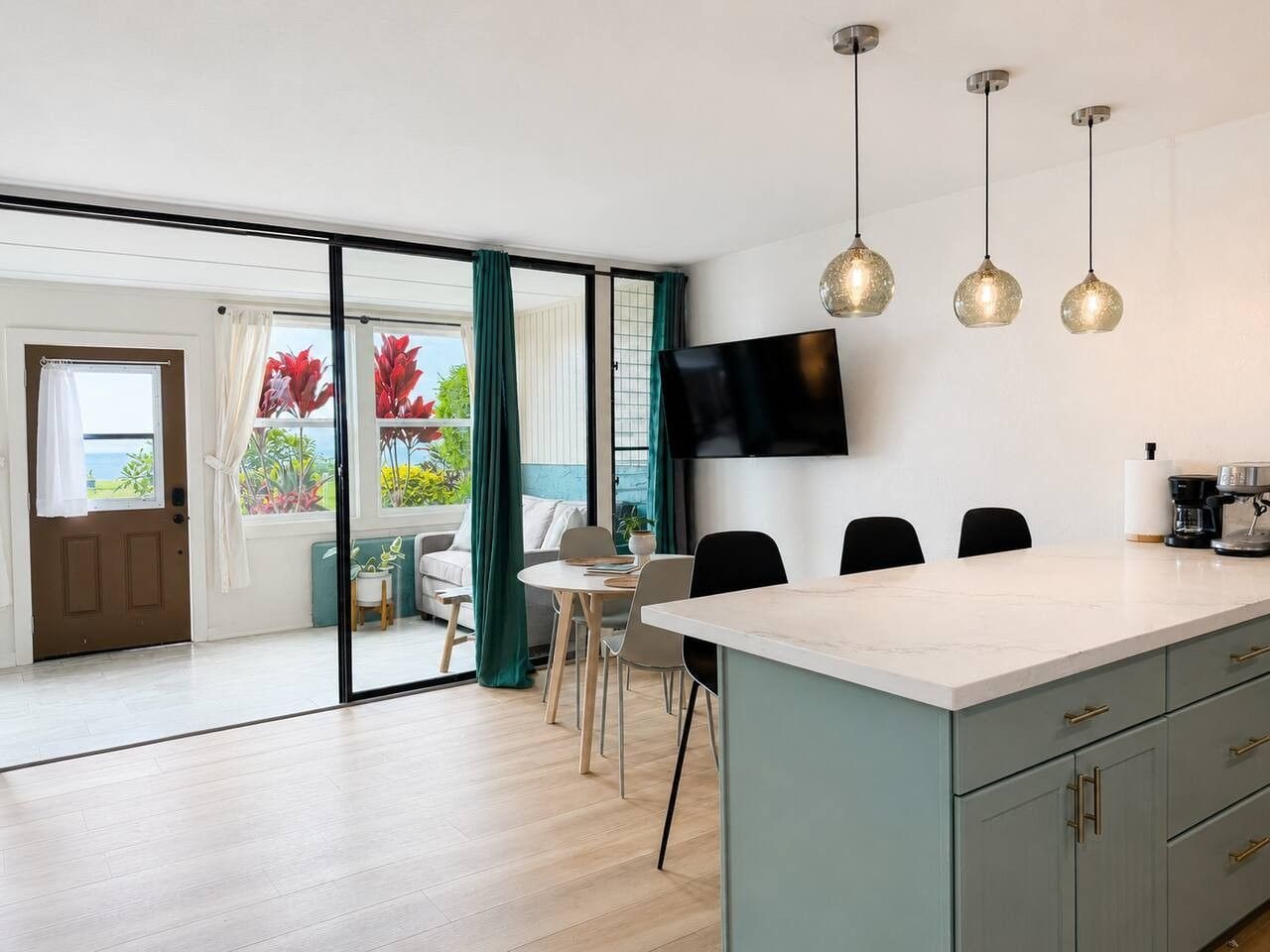 A modern kitchen with a large island, a flat-screen TV, and pendant lights.