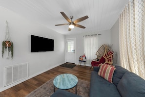 A living room with a ceiling fan, a mounted TV, a sofa, a coffee table, and a wicker chair. - Modern & Bright 2BR Home Near East Lake Park (Birmingham)
