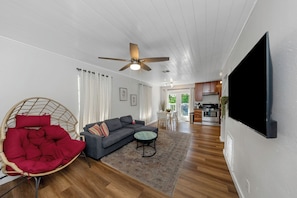 A modern living room with a sofa, a red chair, a ceiling fan, and a flat-screen TV mounted on the wall. - Modern & Bright 2BR Home Near East Lake Park (Birmingham)