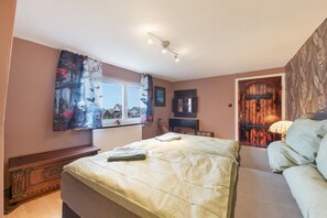 Et soveværelse med seng, kommode, et vindue med gardiner, en dør og en lampe.