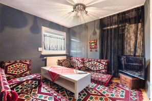 Een woonkamer met een witte zithoek, decoratieve kussens, een televisie en een raam met uitzicht.