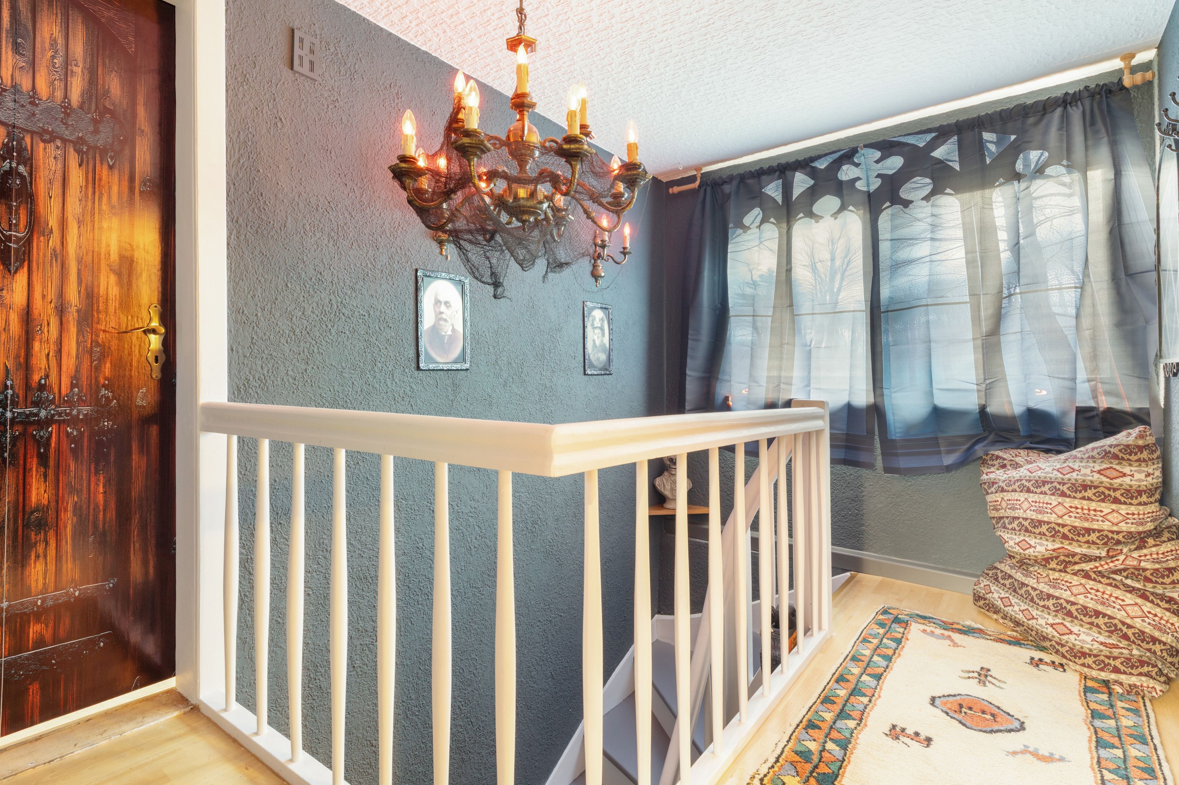 A room with a wooden door, a white railing, a chandelier, and a patterned rug.