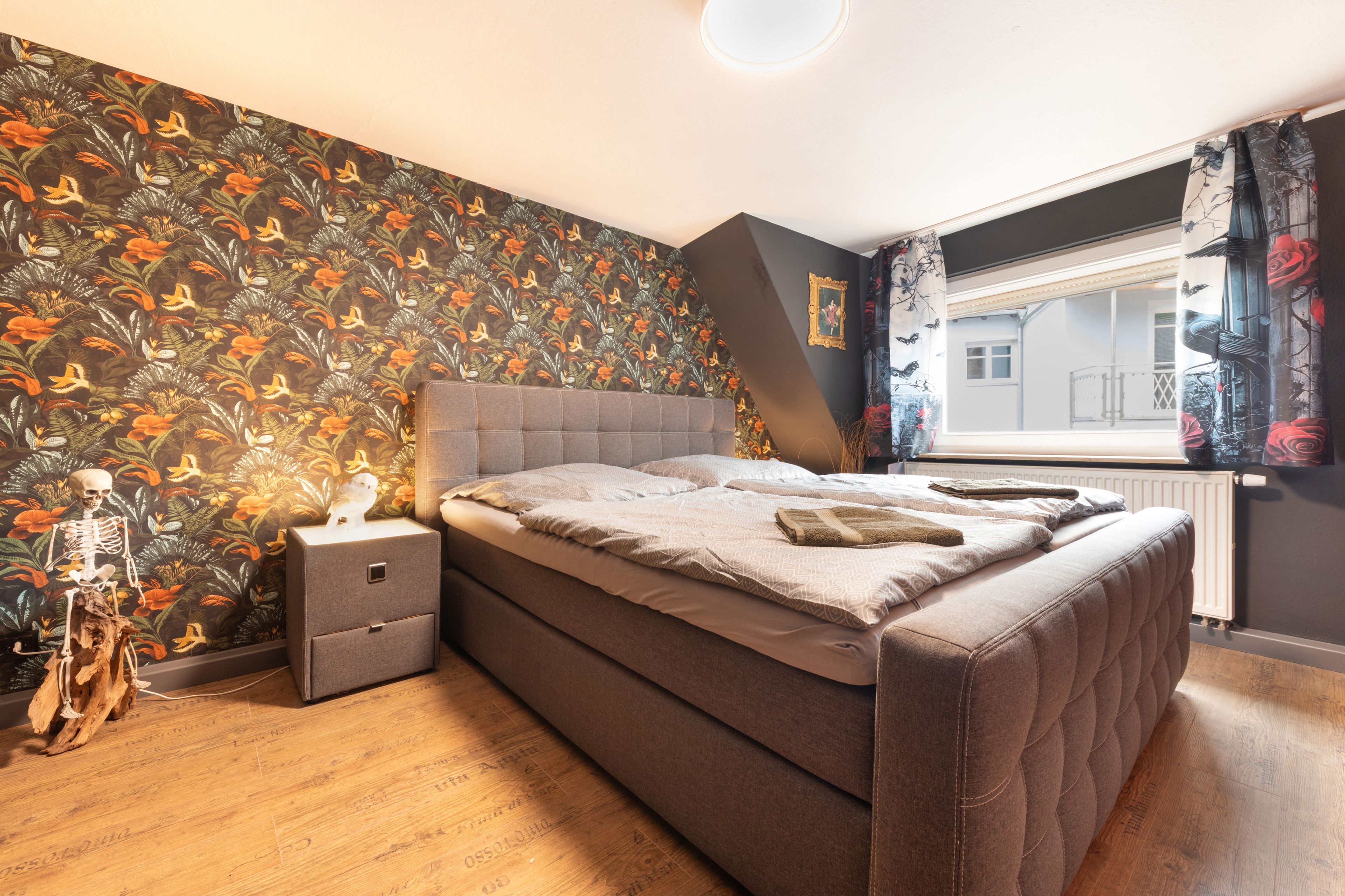 A bedroom with a bed, nightstand, and a decorative skeleton.