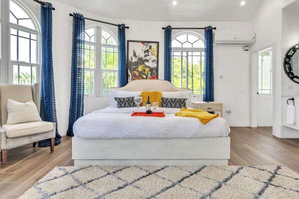 Um quarto espaçoso com uma cama grande, uma cadeira e uma janela com cortinas.