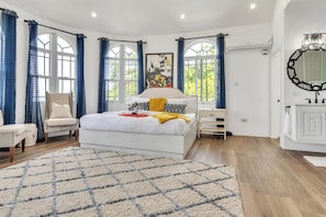 Quarto com cama, cadeira, mesa de cabeceira, janela com cortinas e ar condicionado fixado na parede.