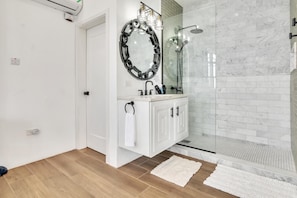 Um banheiro moderno com box de vidro, azulejos de mármore branco e piso de madeira.