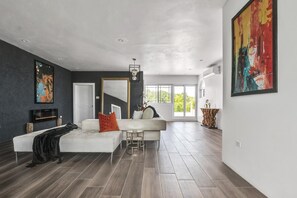 A modern living room with a sofa, a coffee table, and a TV. There is a large window with a view of greenery outside. - Luxury 4 bedrooms with pool and free airport pick up. (Hopewell)