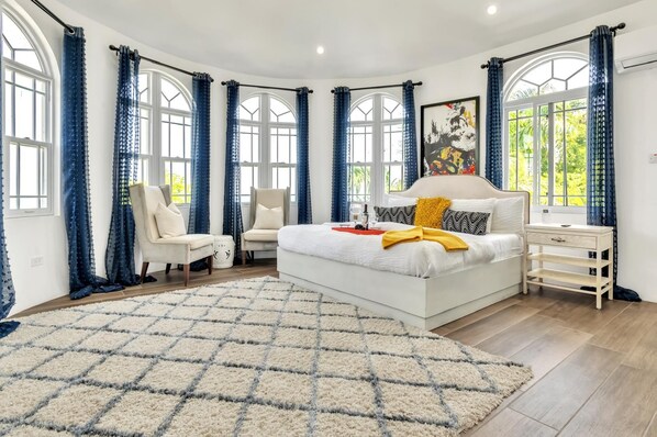 A bedroom with a large bed, two chairs, a bedside table, and a rug. - Luxury 4 bedrooms with pool and free airport pick up. (Hopewell)