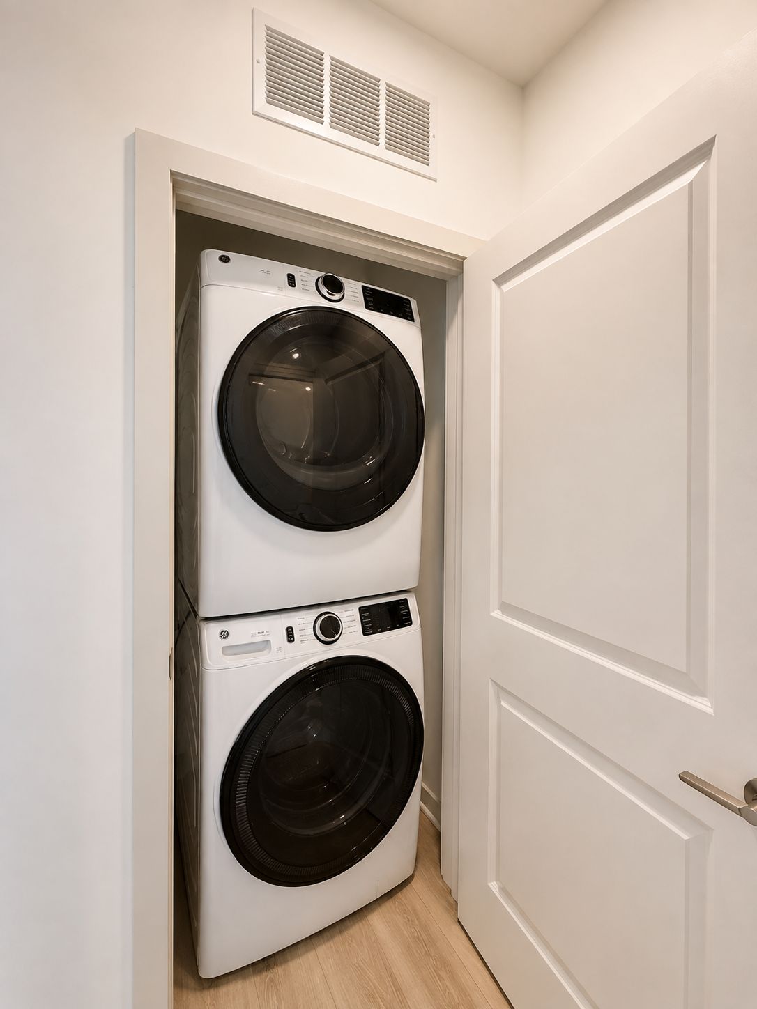 A laundry room with two stacked front-loading washing machines and a door to the right.