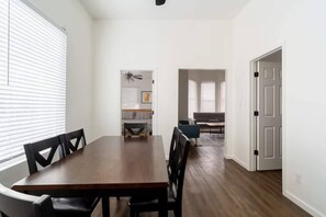 Ein Essbereich mit Holztisch und Stühlen, einem Deckenventilator und Blick in ein Wohnzimmer mit einer Couch und einem Teppich.
