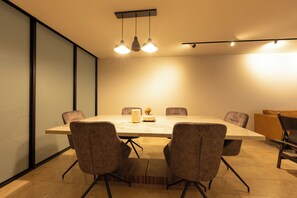 Une salle de conférence avec une table rectangulaire, six chaises, une plante en pot et des luminaires suspendus.