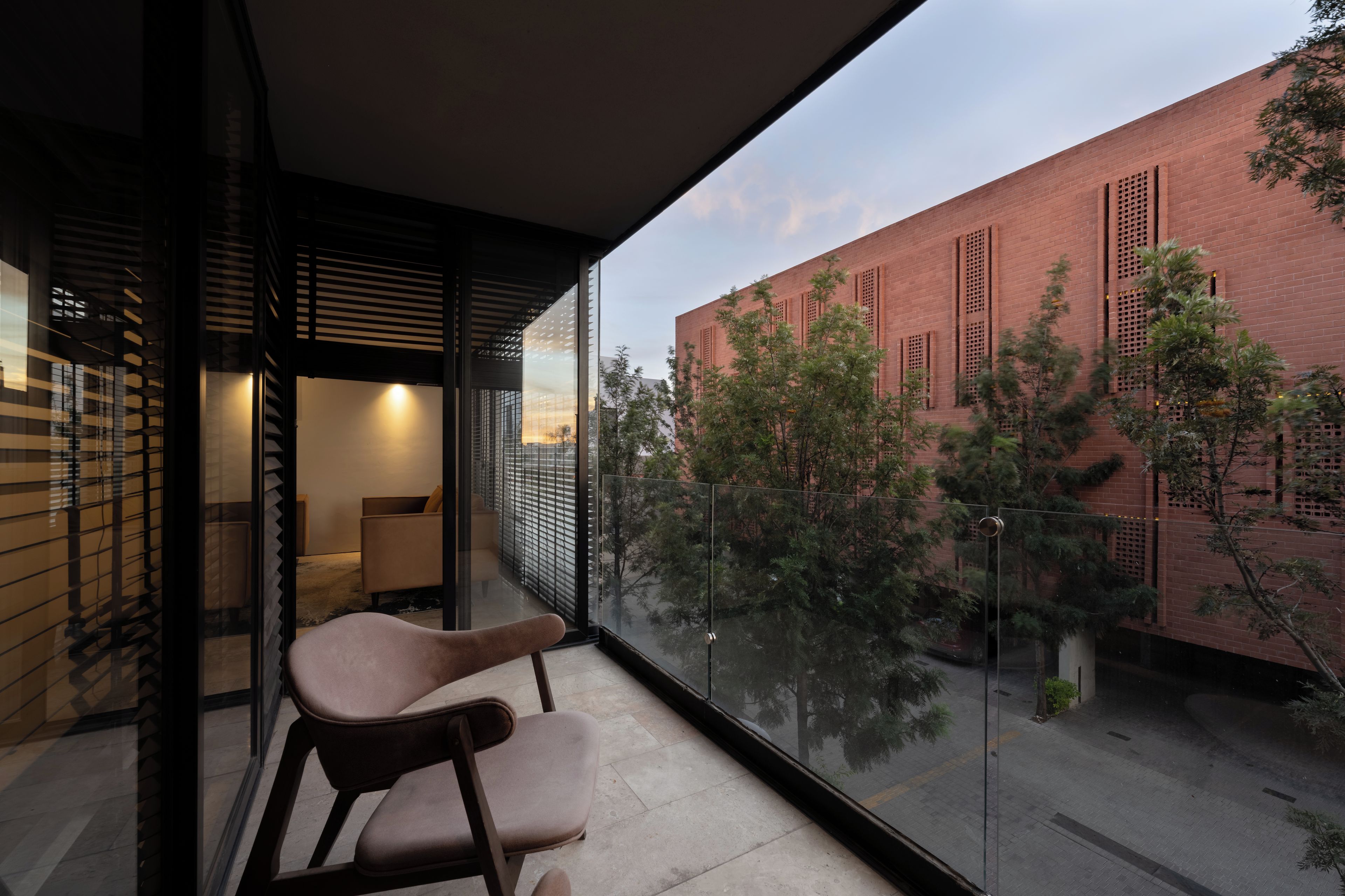 Een modern balkon met glazen hekwerk, met uitzicht op een bakstenen gebouw en bomen.
