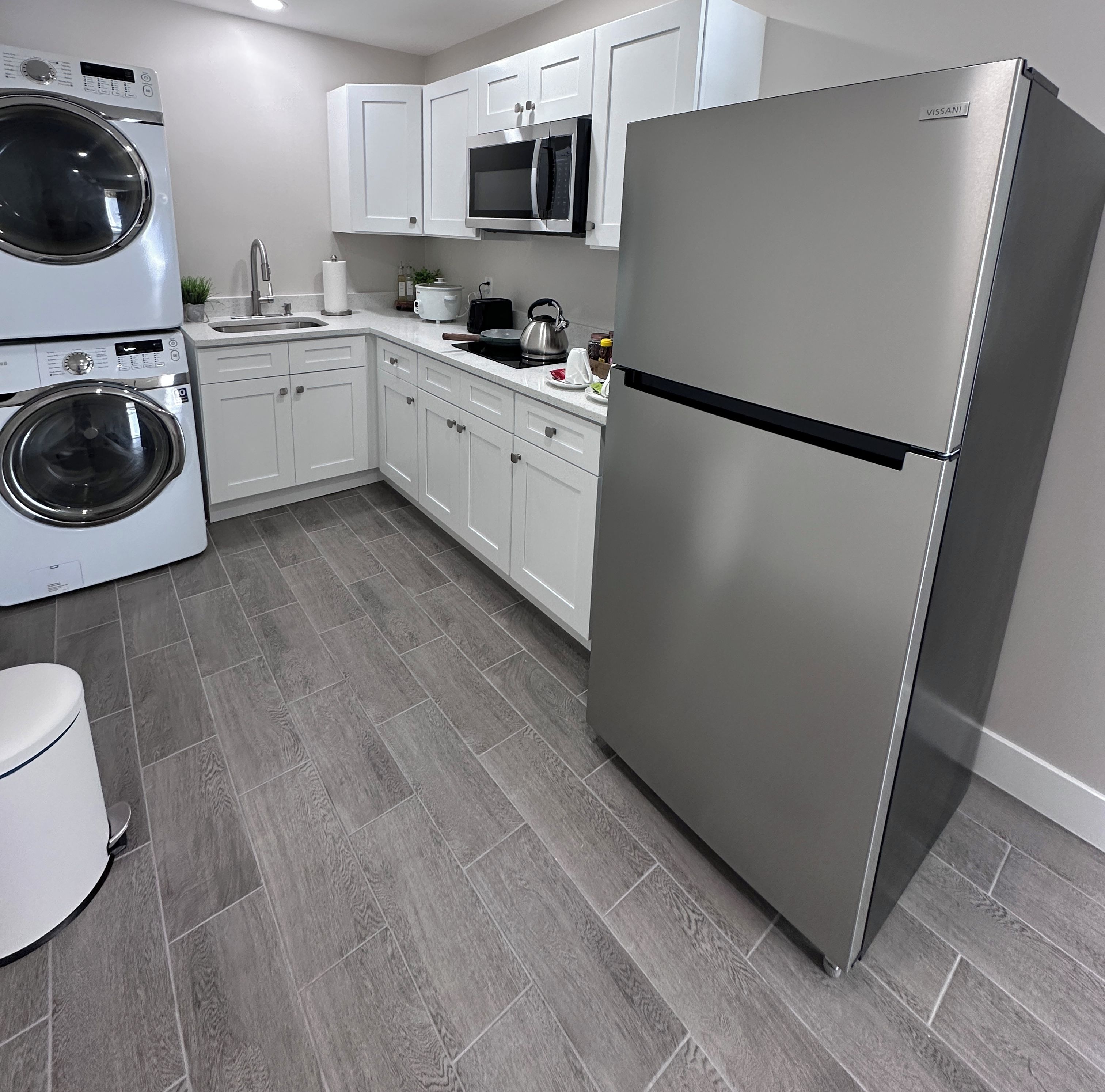 A modern kitchen with stainless steel appliances, white cabinetry, and a grey tiled floor.