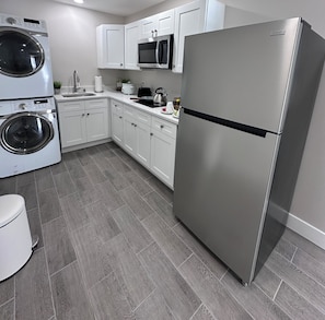 A modern kitchen with stainless steel appliances, white cabinetry, and a grey tiled floor.