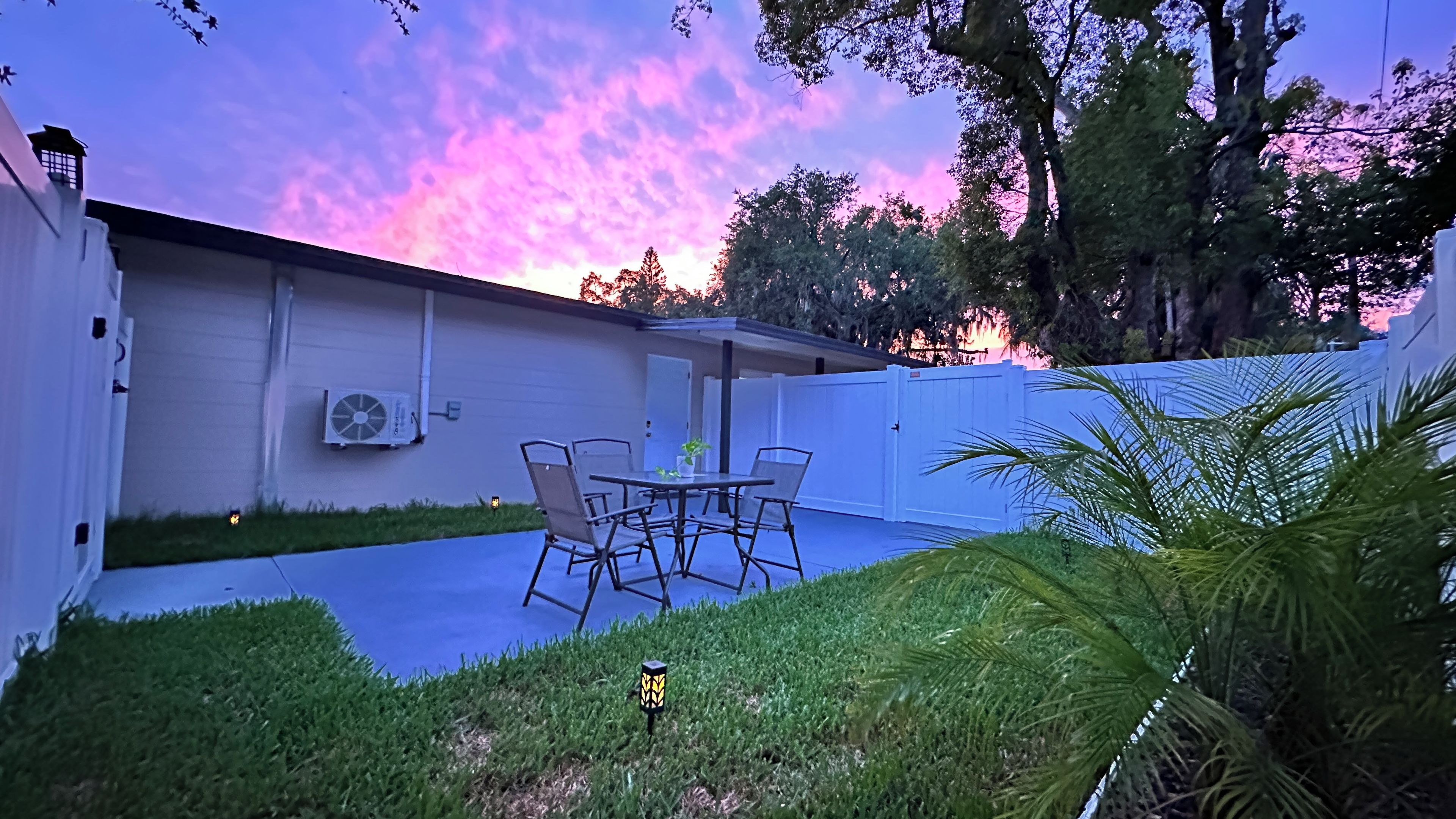 A patio with a table and chairs, a white fence, and a lawn.