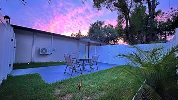 A patio with a table and chairs, a white fence, and a lawn.