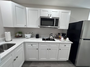 A modern kitchen with white cabinets, a stainless steel refrigerator, a microwave, a kettle, and a coffee maker.