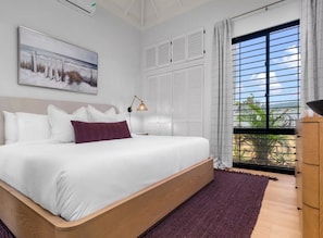 A bedroom with a large bed, a painting on the wall, a window with shutters, and a view of the outdoors. - 5BR Runaway Bay Villa with private Pool  (Runaway Bay)