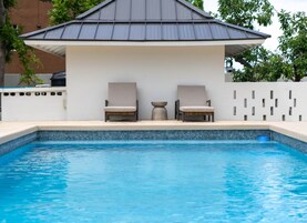 Piscina con dos sillas de descanso y una zona de estar cubierta.