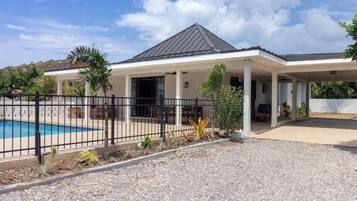A residential property with a swimming pool, covered patio, and a fenced garden area.