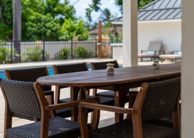 Una mesa de madera con seis sillas, una lámpara de mesa pequeña y una vista a una piscina y follaje al fondo.