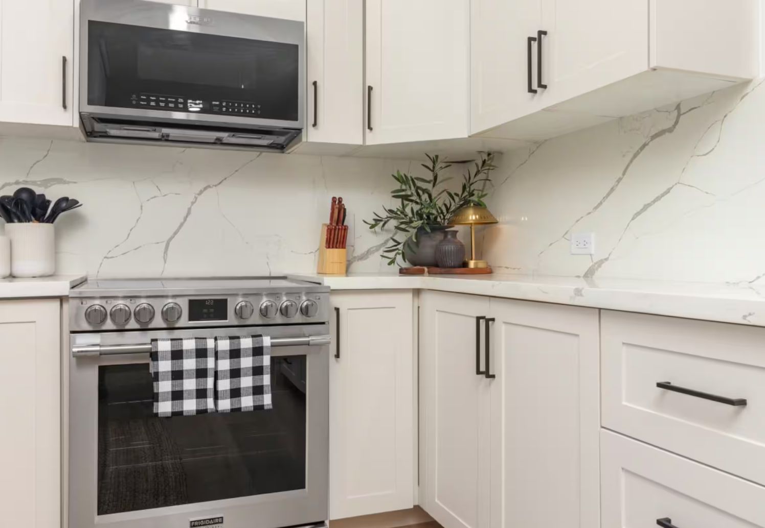 A kitchen with white cabinets, a stainless steel oven, a microwave, and a checkered towel hanging on the oven door.