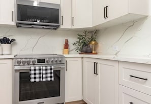 Une cuisine avec des armoires blanches, un four en acier inoxydable, un four à micro-ondes et un torchon à carreaux accroché à la porte du four.