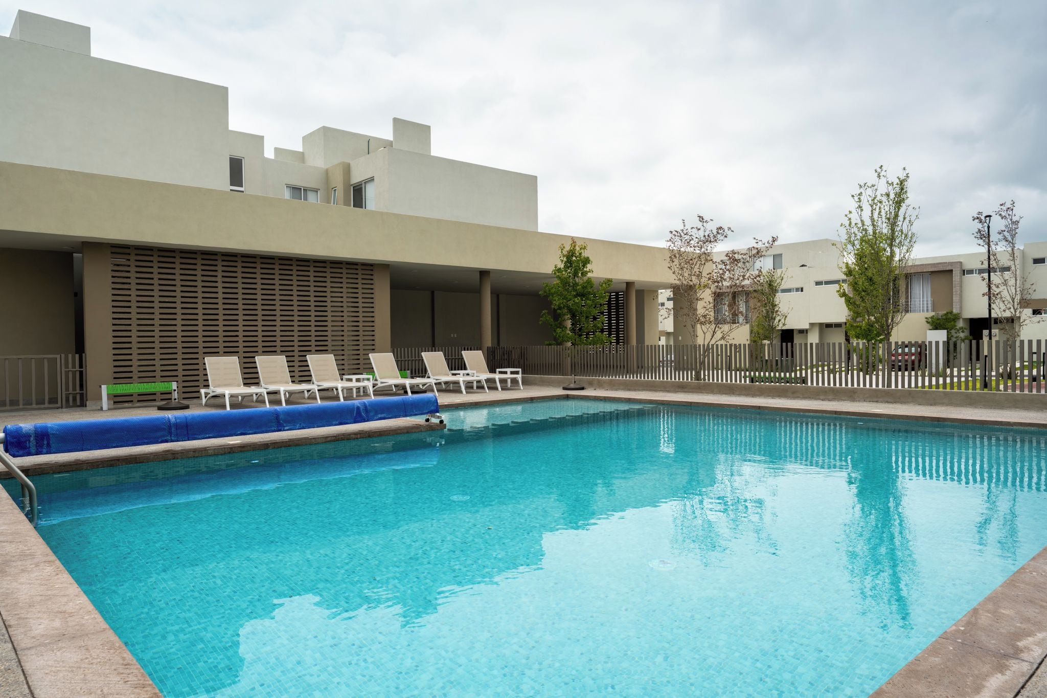 A swimming pool with lounge chairs and a fence.