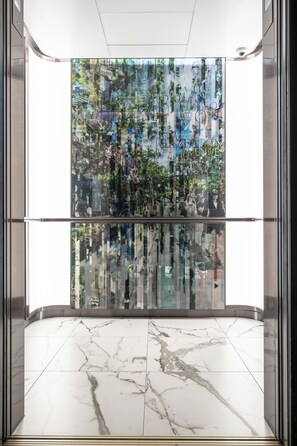 Un ascensor moderno con un muro de vidrio reflectante que muestra un paisaje urbano.