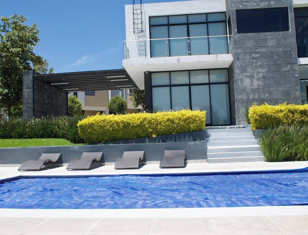 Un bâtiment moderne doté d’une piscine, de chaises longues et d’un jardin bien entretenu.