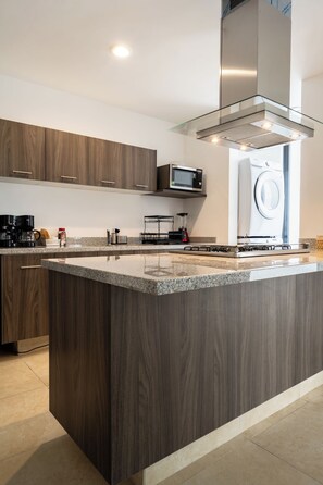 Cozinha moderna com ilha central, micro-ondas embutido e coifa de aço inoxidável.