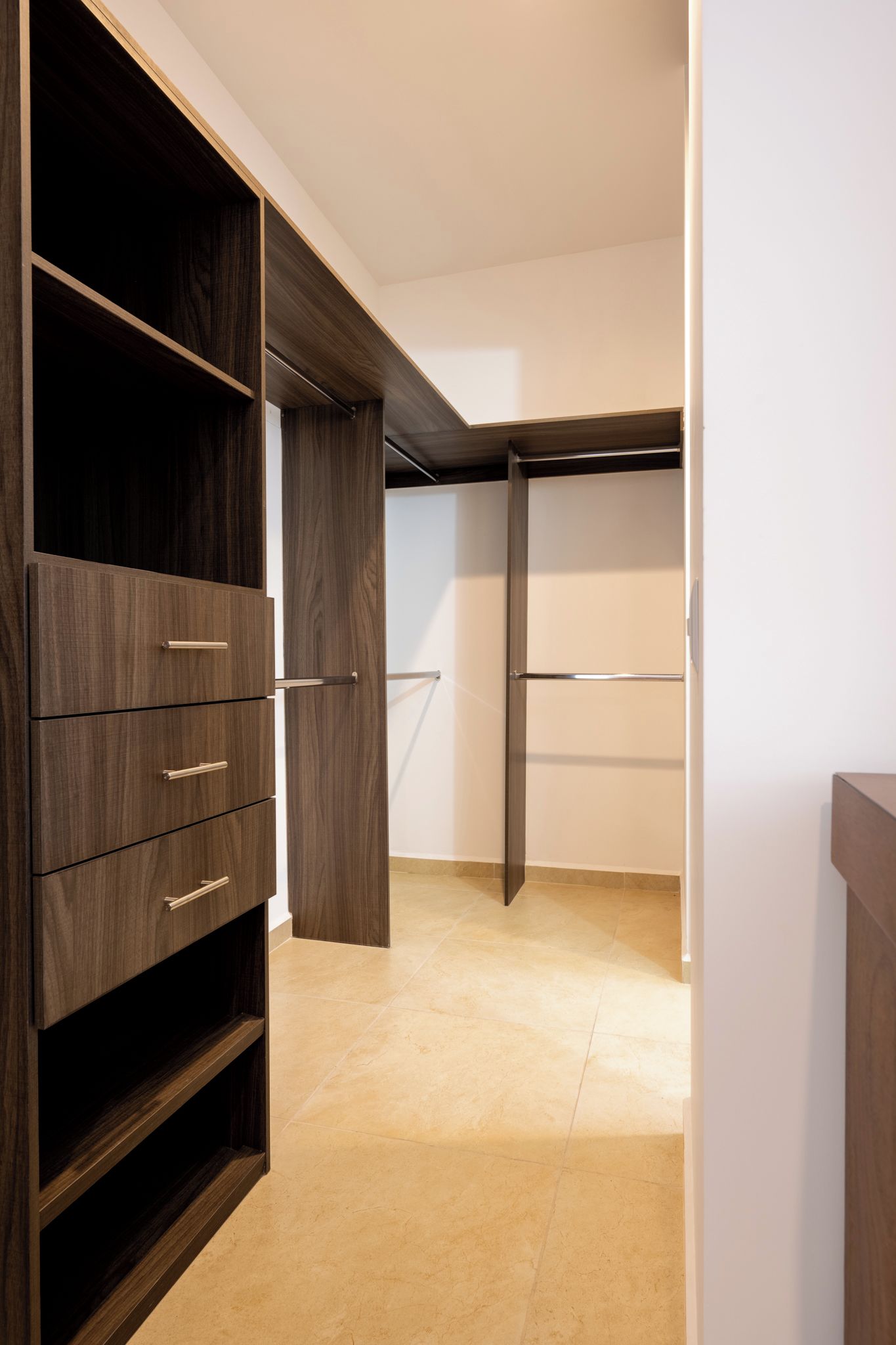 Un dressing accessible sans porte, avec des étagères et des tiroirs en bois, un sol carrelé et un mur blanc.