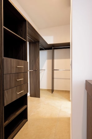 Un dressing accessible sans porte, avec des étagères et des tiroirs en bois, un sol carrelé et un mur blanc.