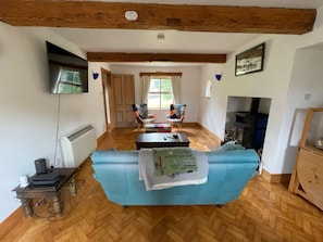 Un salon avec un canapé bleu, un plancher en bois, une cheminée et un téléviseur fixé au mur.