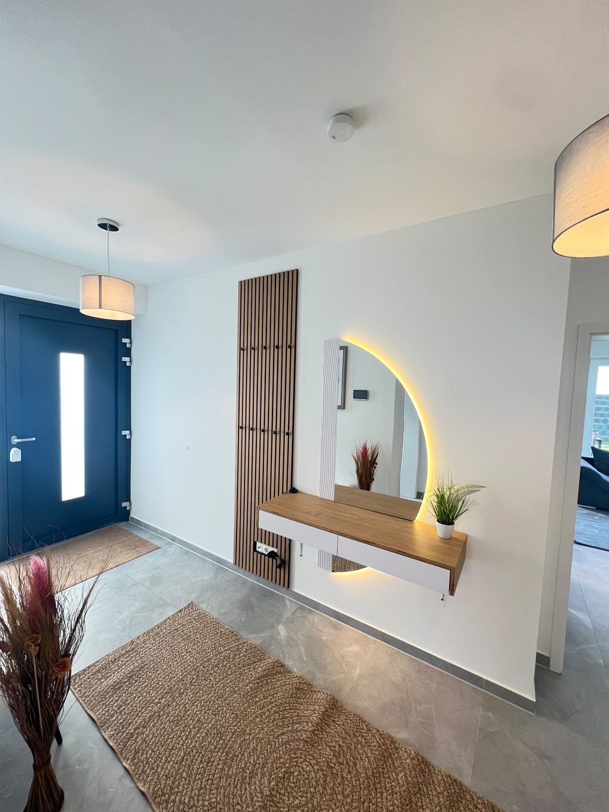A modern interior with a wooden console, a mirror with a curved frame, and a blue door.